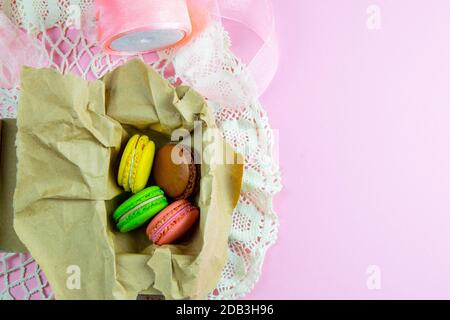 Yellow, pink, green and brown macaroons in the craft pack on pinc background. Top views with clear space Stock Photo