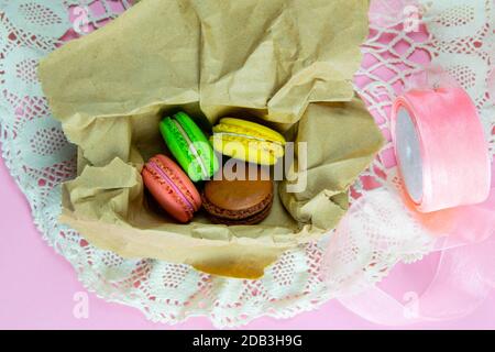 Yellow, pink, green and brown macaroons in the craft pack on pinc background. Top views Stock Photo
