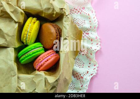 Yellow, pink, green and brown macaroons in the craft pack on pinc background. Top views with clear space Stock Photo
