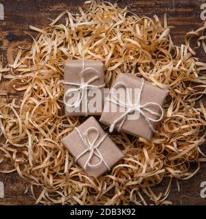 Three small gifts are wrapped in kraft paper and lay in wood shavings. Handmade gift concept, eco-friendly packaging. Rustic style. Top view Stock Photo