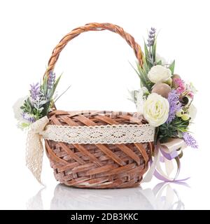 Wicker brown basket decorated with delicate colored flowers of pastel colors and ribbons on white background. Made in a rustic style Stock Photo