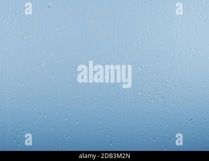 Close up raindrops and water runs on glass window pane surface over grey and blue sky background on rainy day Stock Photo