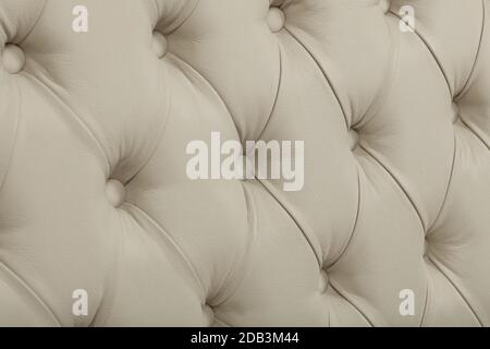 Close up background texture of beige white capitone genuine leather, retro Chesterfield style soft tufted furniture upholstery with deep diamond patte Stock Photo