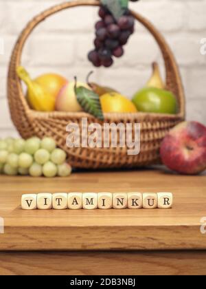 Small wooden blocks with the German word Vitamin cure on a kitchen table with fresh fruits in the background, healthy food concept Stock Photo