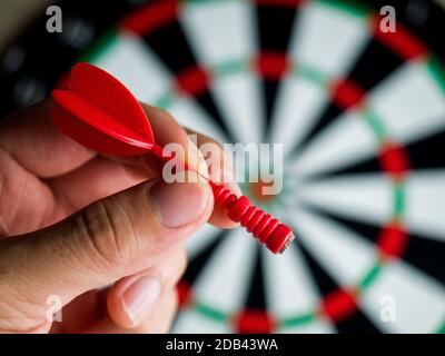 A closeup shot of a hand holding a red dart in front of a dartboard Stock Photo