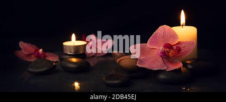 spa and alternative therapy. candles with massage stones and orchid flowers on black background. banner Stock Photo
