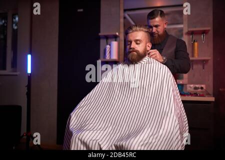 handsome caucasian man at the hairdresser in barber shop, barber male trimming hair to customer with electric razor at barbershop Stock Photo