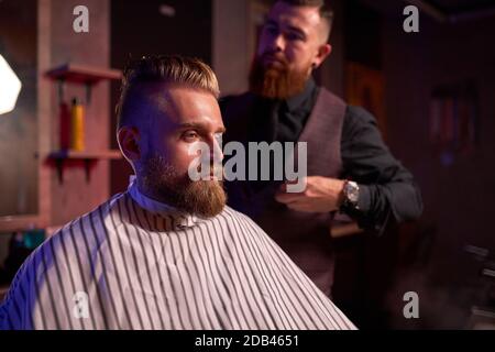 confident male hairstylist cut hair to elegant stylish man sitting in salon, young male enjoy the process of cutting Stock Photo