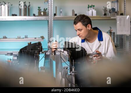 engineer measures plastic components for the production of lights for the automotive industry in a factory on a digital 3D machine. Stock Photo
