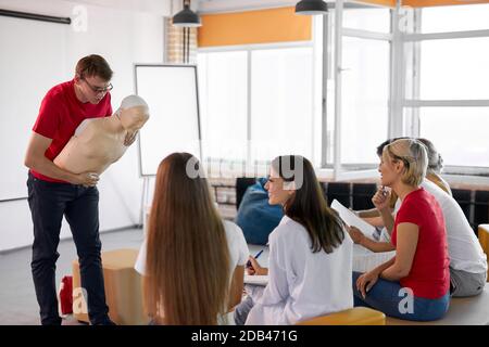 CPR class with male instructor speaking and demonstrating help, giving lessons of first aid. compression and resuscitation procedures. Cpr mannequin is used for an example Stock Photo