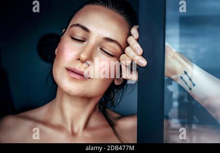 Portrait of a beautiful woman in a dreamy mood with closed eyes standing near the window at home, genuine beauty of a young female Stock Photo