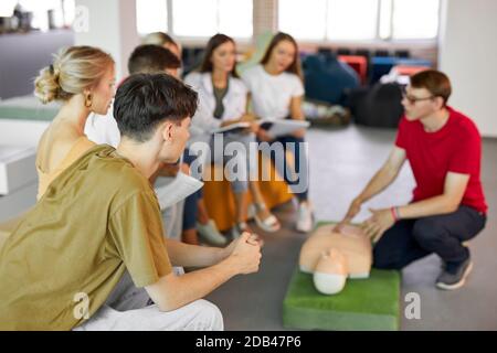 CPR class with male instructor speaking and demonstrating help, giving lessons of first aid. compression and resuscitation procedures. Cpr mannequin is used for an example Stock Photo