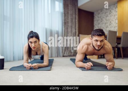 Morning fitness workout of family couple at home. Active man and woman in sportswear doing push up exercise in their house, healthy lifestyle, physica Stock Photo