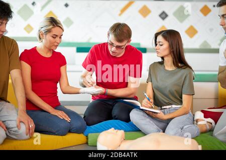 young male instructor show how bandage a hand in a right way, group of people learn the first aid techniques Stock Photo