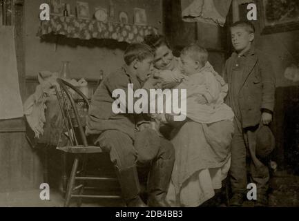 Flash light photo of John Sousa, his mother and some brothers and sisters. John is sitting. Crowded, dirty home. . Stock Photo