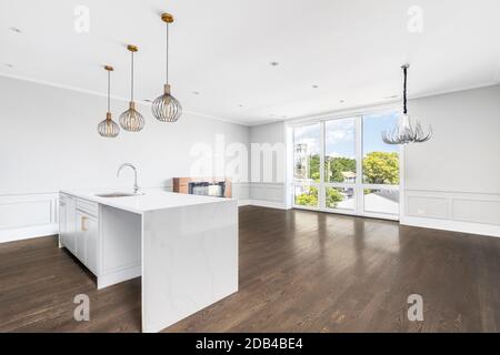 An empty, luxurious kitchen, dining room, and living room with gold lights, a fireplace, and chandelier above the hardwood floors. Stock Photo