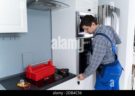 Male Technician In Overall Installing Oven In Kitchen Stock Photo