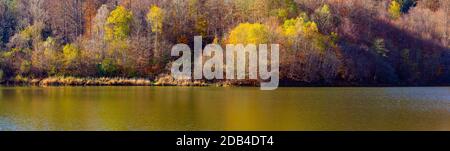 Panorama of autumn trees reflecting in calm waves of a lake Stock Photo