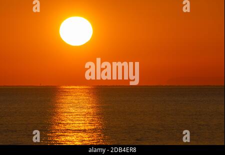 Landscape view of low sun setting, showing sunset over the sea with a clear reflection in the water. Stock Photo
