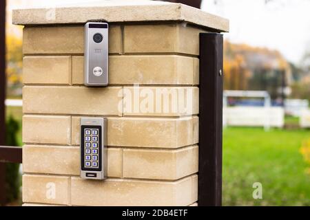 Silver intercom call panel with blue number buttons and a video camera on a brick beige fence post of a private house Stock Photo