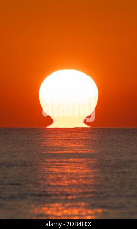 Portrait of a low sun setting over the sea. Vertical of sunset over the ocean with sun touching the water.