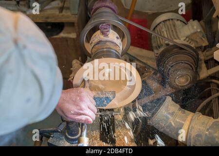 Making a wooden bowl on a lathe in an old small workshop with flying wooden shavings Stock Photo