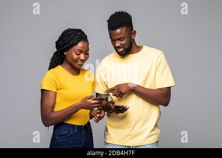 Concentrated young african american couple standing with smartphones in hands, busy with chatting in social networks, using mobile apps, websurfing in Stock Photo