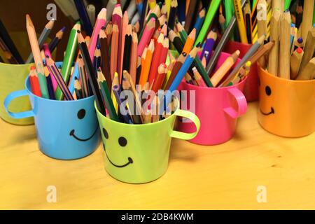 Close view of colored pencils on smiley cups on a school. Stock Photo