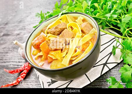 Central Asian national dish Lagman of meat, noodles and vegetables in bowl on a napkin, garlic, parsley on black wooden board Stock Photo