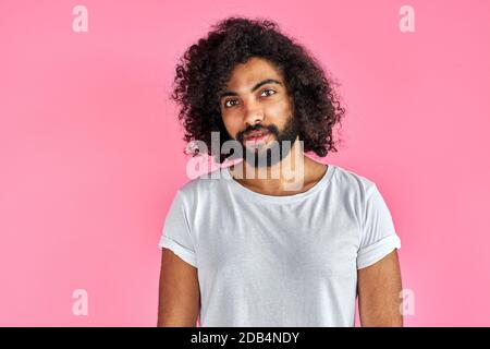 portrait of pleased arab man isolated in studio, handsome guy in casual wear posing at camera, has black long curly hair, calm male of indian or arabian appearance Stock Photo