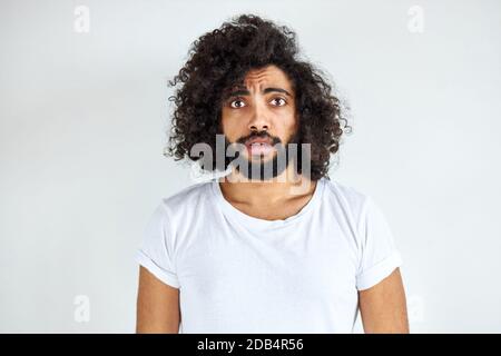 scared curly arabian young guy stand in fear by something, look at camera, isolated over white background. Stock Photo