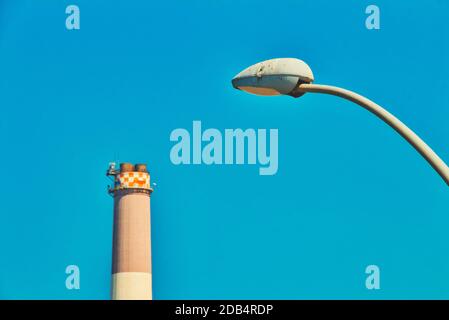 Close up on modern street lamp post and Reading power plant chimney in the background on a sunny day at Tel Aviv city. Concept of industry, pollution, Stock Photo
