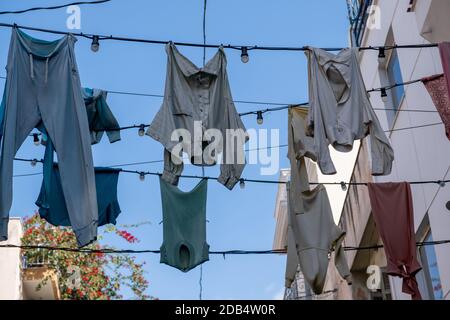 Shabby garments hanging and drying on electric cables with light bulbs against blue sky in Monastiraki street. Athens Greece. Cloths natural old fashi Stock Photo