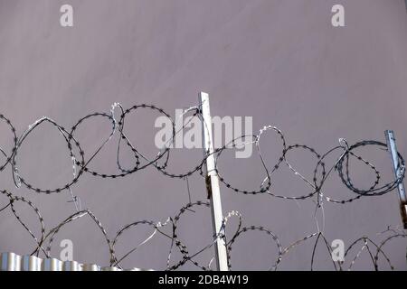 From below metal fence with barbed wire on top located against gray wall on street Stock Photo