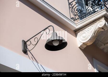 Old fashioned lamp on a neoclassical building facade, Athens Greece. Ornamental retro lantern hanging on wall near balcony over entrance of building o Stock Photo