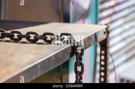 Locked with safety. Weathered chain placed on metal table blur garage roller shutter background, , closeup view. Sunny day on town street. Stock Photo