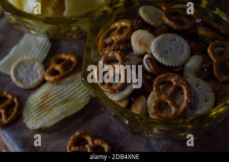 Various mix of salty snacks with wavy potato chips, pretzel and crackers in a bowl and on a wooden table Stock Photo