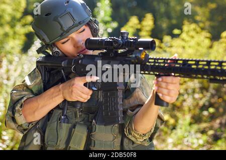 sportive caucasian woman soldier shooting with rifle machine gun in the forest, young slim female is hunting Stock Photo