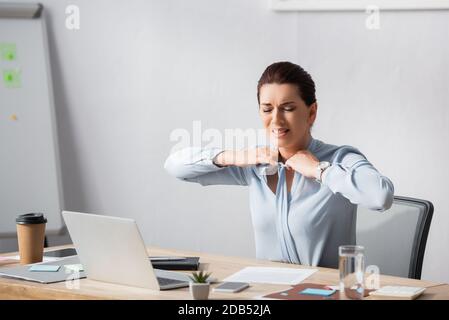 Irritated businesswoman untying blouse while sitting at workplace in office Stock Photo