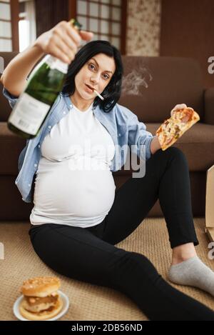 Pregnant woman with belly smoking and drinks beer at home. Pregnancy ...