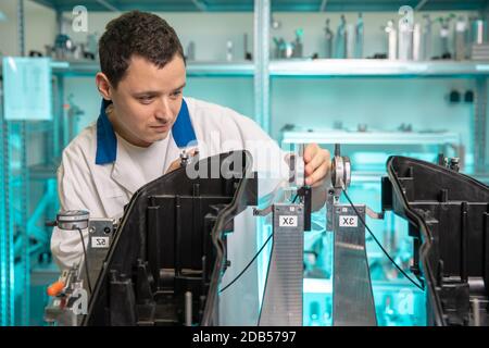 engineer measures plastic components for the production of lights for the automotive industry in a factory on a digital 3D machine. Stock Photo