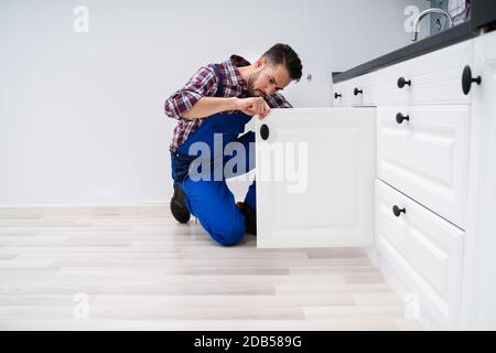 Young Handyman Fixing Sink Door In Kitchen Stock Photo