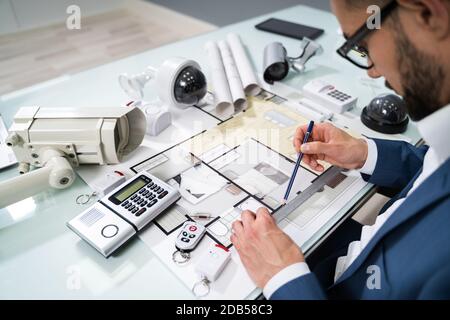 Architect Drawing Blueprint With Various Security Equipment On Desk Stock Photo