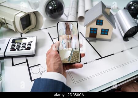 Person Hand Using Home Security System On Mobilephone With On Blueprint With Security Equipment Stock Photo