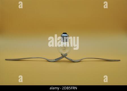 light bulb balancing on composition of 2 intertwined forks isolated on orange neutral background, conceptual photo to indicate division of electricity Stock Photo