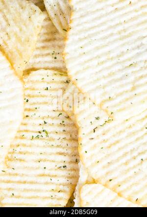 a bunch of yellow and crispy , sprinkled with green spices, potato chips, rippled , abstract background closeup Stock Photo