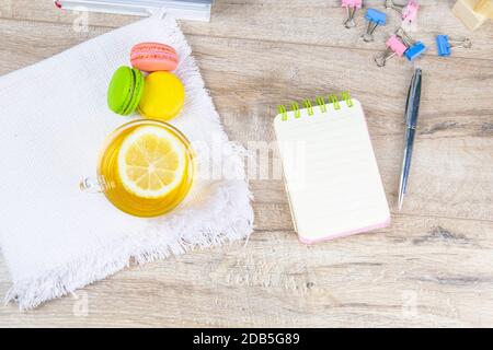 An open notebook with a silver pen, a cup of mint tea with lemon and multi-colored muffins stand next to it. Stock Photo
