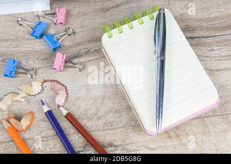 The notebook on which there is a pen of silver and next to pencil sharpening shavings and a few pencils on a wooden table. Stock Photo