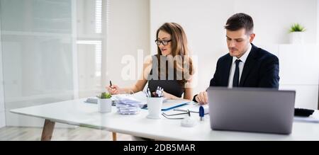 Two Young Businesspeople Calculating Invoice With Calculator Stock Photo