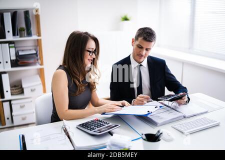 Two Young Businesspeople Calculating Invoice With Calculator Stock Photo